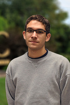 An informal portrait of young researcher, he is outside in front of the u-m-b-c sign