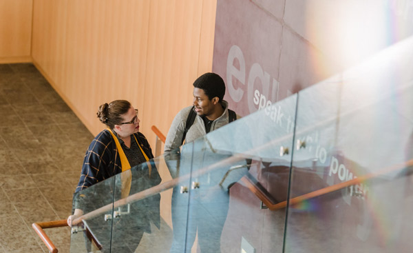 A female and male student standing on a stairway in a discussion