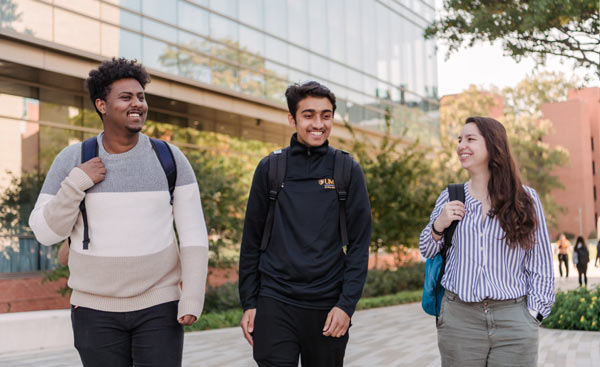 Three students, two me and one woman casually walking down academic row in a discussion